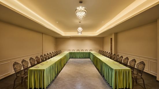 Elegant conference room with U-shaped table arrangement, transparent chairs, green table skirting, and ambient lighting from crystal chandeliers - Voyage The Solitaire Bliss.