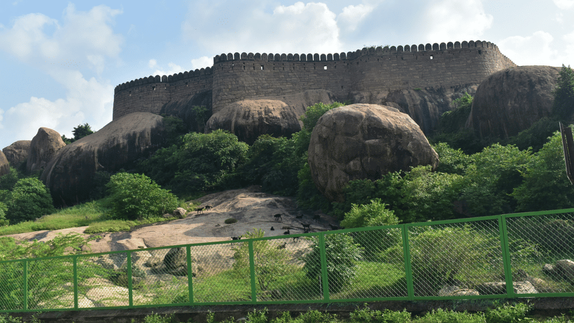 A hilltop fort built over large boulders, with stone walls along the ridge and a fenced path at the base | Chennai to Thirumayam