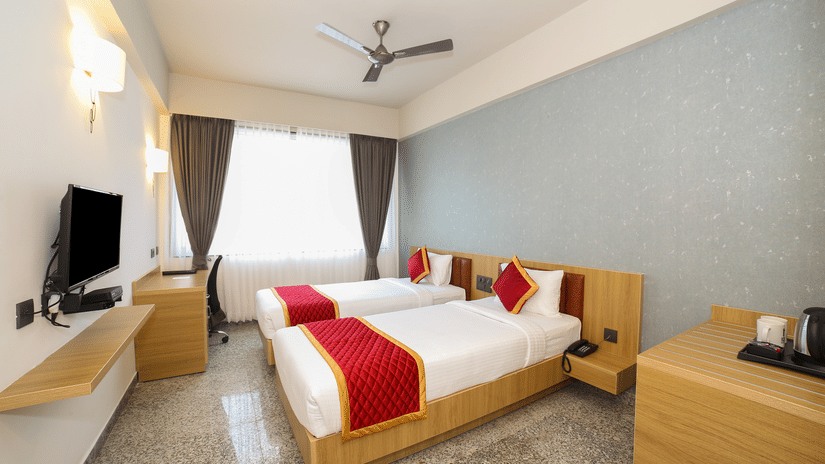Two single beds, a wall-mounted television, and a wooden desk at Icon Express By Bhagini, Mahadevapura.