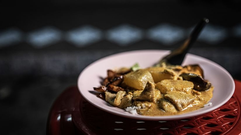 A appetising pork dish on a plate with spoon set on a red chair. 