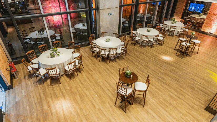 An overhead view of a large room with wood floors, several round tables with white cloths and chairs.