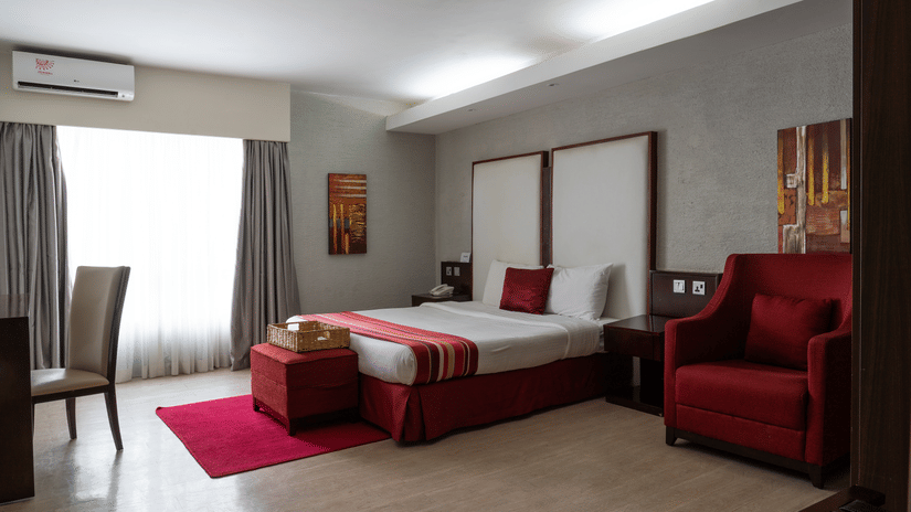 A double bed, a seating area, a writing table, and a ceiling-to-floor window inside the Superior Room at The Zehneria, Nairobi.