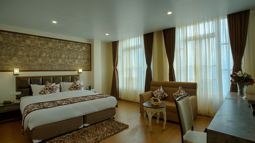 A Deluxe Room at Voyage with a large bed, pillows, spreads, windows covered with curtains, and a sofa.