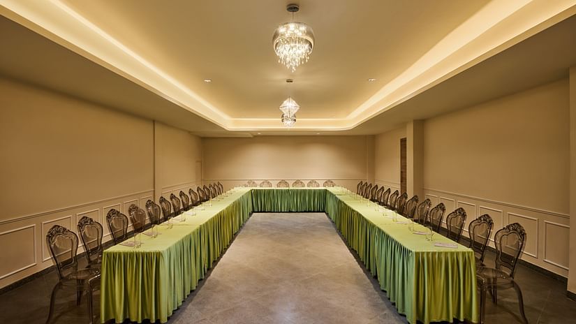 Elegant conference room with U-shaped table arrangement, transparent chairs, green table skirting, and ambient lighting from crystal chandeliers - Voyage The Solitaire Bliss.
