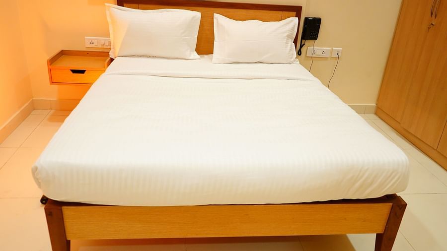 A room with clean bed, side drawers, a dial phone and a wardrobe - A M Suites