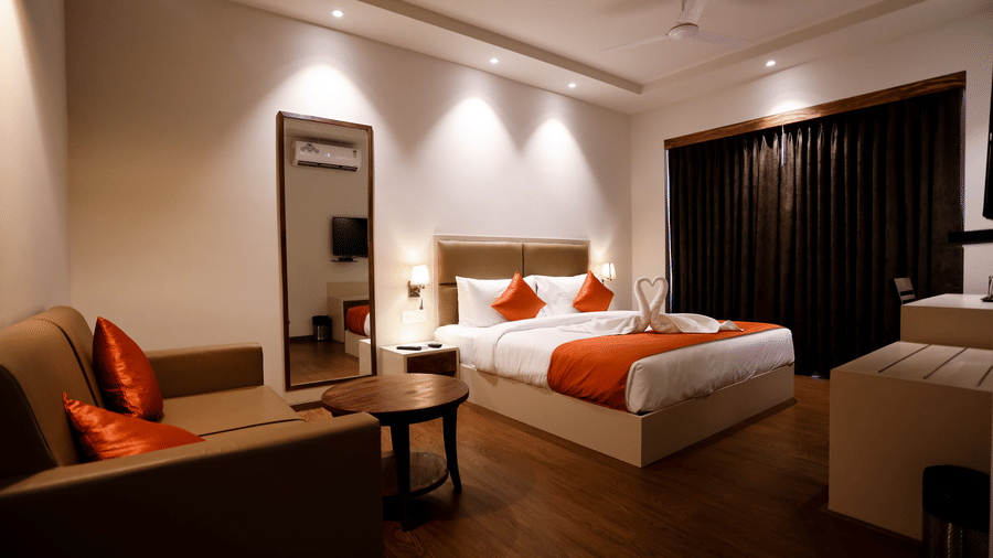 A room with a double bed, a seating area, and a mirror beside it at Amara Grand Baga, Goa.