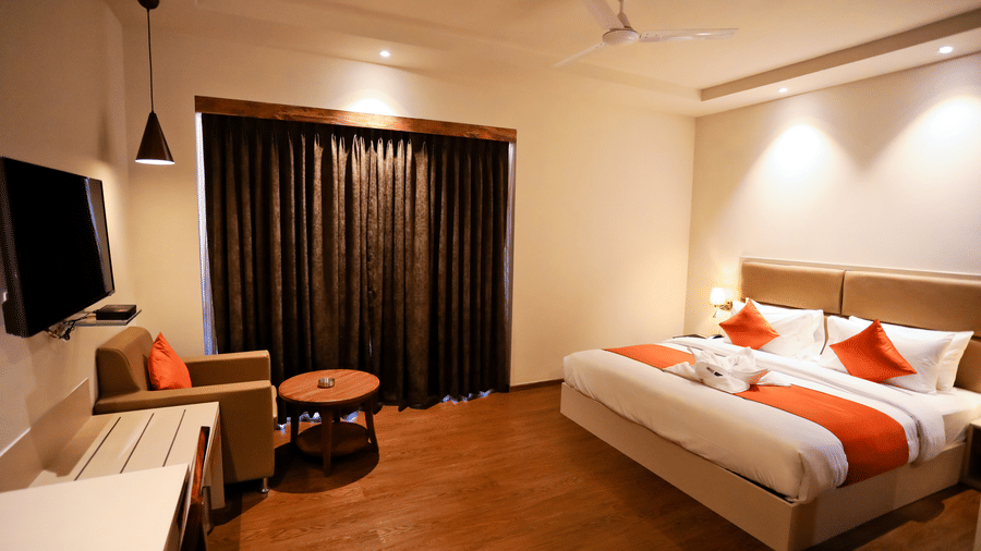 Spacious room with a bed and a television in front and a seating area on the side at Amara Grand Baga, Goa.