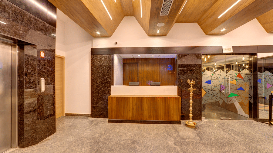 A wooden reception desk, an elevator, and a wooden slatted ceiling in the lobby of Icon Express By Bhagini, Hoodi.