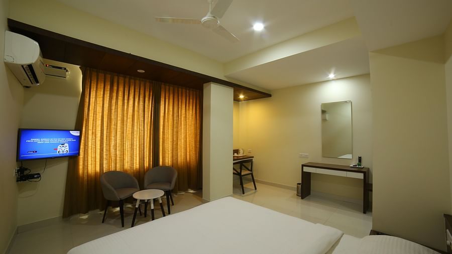 Mysore Gate Hotel, Bangalore Bengaluru A room featuring a neat bed a smart TV a vanity area sofa chairs and a table - Mysore Gate Hotel Bangalore