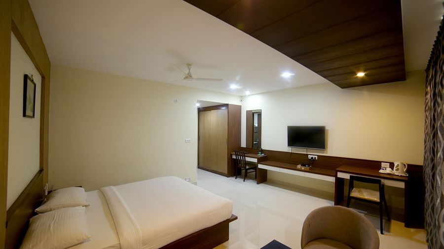 Mysore Gate Hotel, Bangalore Bengaluru A room featuring a wooden bed a sofa chair a vanity area and a TV - Mysore Gate Hotel Bangalore