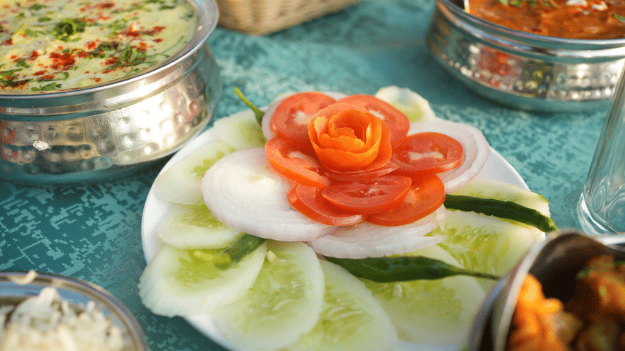 A close up shot of a salad based out of tomatoes, onions and cucumber, along with a view of other dishes on the table | Sol Glow Resort, Nainital