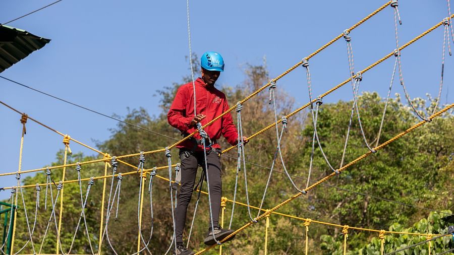 Person participating in a rope bridge adventure activity in a forest setting. | Stone Wood Jungle Resort, Dandeli