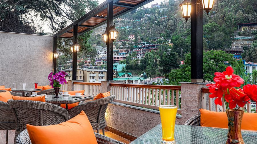 A rooftop cafe with lanterns, vibrant pillows, chairs and tables, all overlooking a scenic mountain view -  Vinsober Monal, Nainital