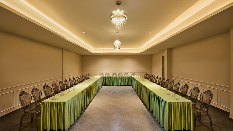 Elegant conference room with U-shaped table arrangement, transparent chairs, green table skirting, and ambient lighting from crystal chandeliers - Voyage The Solitaire Bliss.