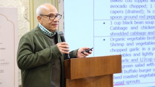 An image of a man standing on a podium with a microphone in her hand giving a speech at Heritage Village Resorts & Spa