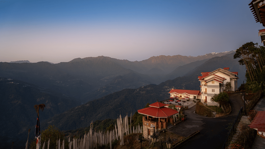 The aerial view of Summit Norbu Ghang - The Signature Collection, Gangtok, showing surrounding mountains and nearby buildings at dusk.