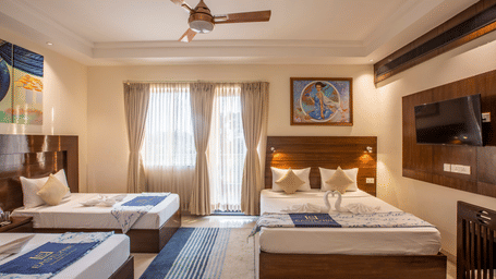 A spacious family-style room with 3 separate beds, blue striped rugs, and large windows for natural light — Eastlynn Resort, Rishikesh