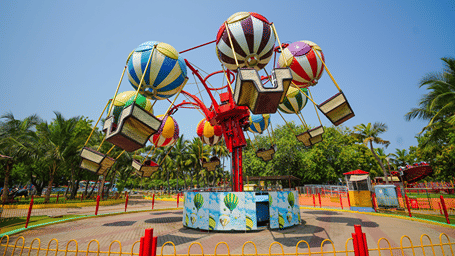 Balloon Race ride with striped hot-air-balloon canopies over hanging baskets on red arms, inside a yellow fence at MGM Dizzee World, Chennai.