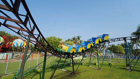 Reindeer Coaster with a reindeer-head front car and blue and yellow carriages on a green steel track above a lawn at MGM Dizzee World, Chennai.
