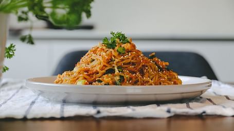 A plate consisting of Pad Thai placed on a table with a small plant in the background.