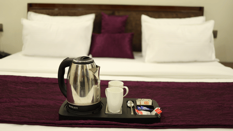 A bedroom at Perfectstayz Value Forest Valley, with a king size bed, pillows, and a tray with an electric kettle, 2 mugs, a spoon, and sachets.