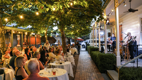 A festive setting at Tallman Hotel featuring events in Northern California, where guests gather outdoors in groups to enjoy live music on the porch of a historic building.