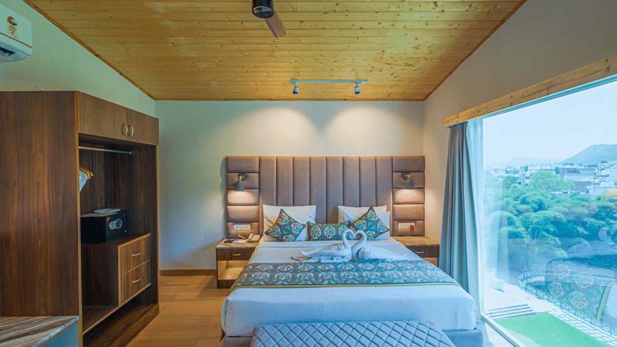 A stylish room with a large window overlooking a landscape, a large bed, and modern furnishings at Bamboo Saa Resort & Spa, Udaipur.