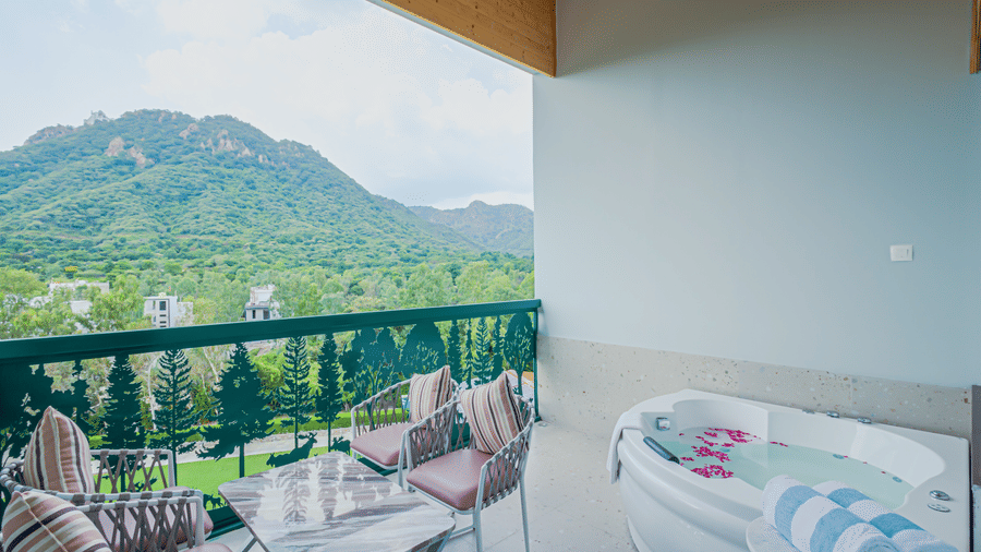 An outdoor balcony with a small bathtub, seating area, and a railing overlooking hills at Bamboo Saa Resort & Spa, Udaipur.