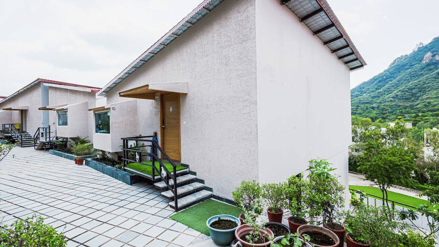 The exterior of a modern building with a paved courtyard and potted plants on a bright day at Bamboo Saa Resort & Spa, Udaipur.
