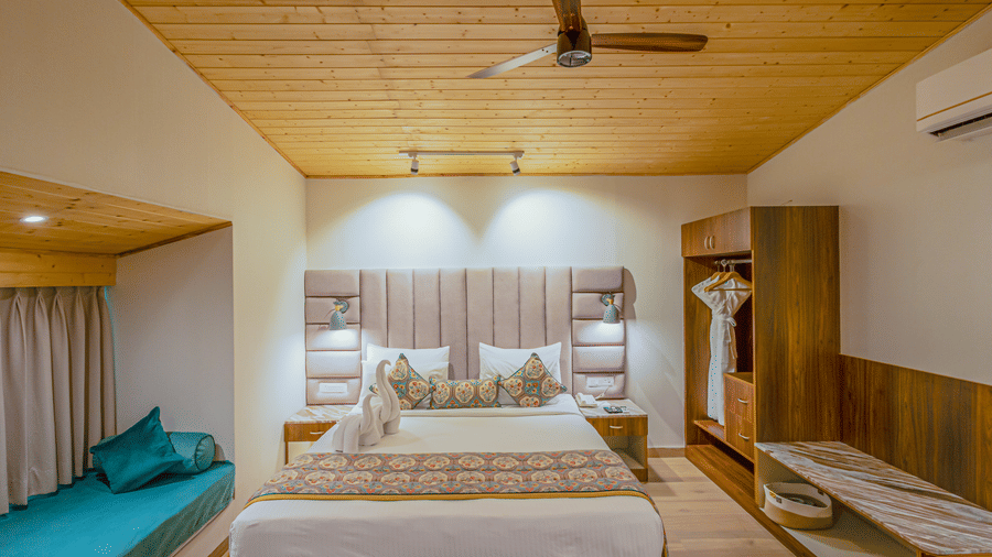 A comfortable bedroom featuring a large bed, seating area near the window, and wooden panelling at Bamboo Saa Resort & Spa, Udaipur.