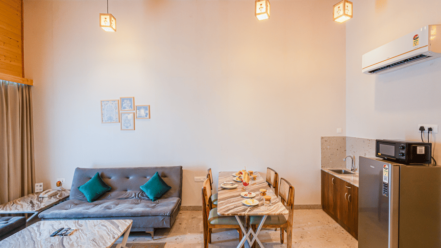 Living area at Sajjan Villa featuring a sofa set with centre table and a dining table with chairs. The room also features a refrigerator,  oven, a sink.