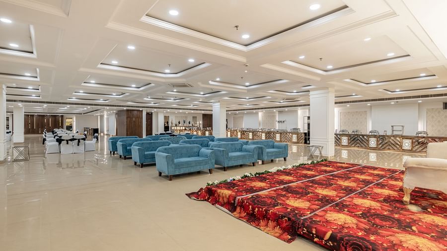 Versatile event hall with soft lighting, blue sofas, and red carpeted section at Hotel Highway King, Bilaspur.