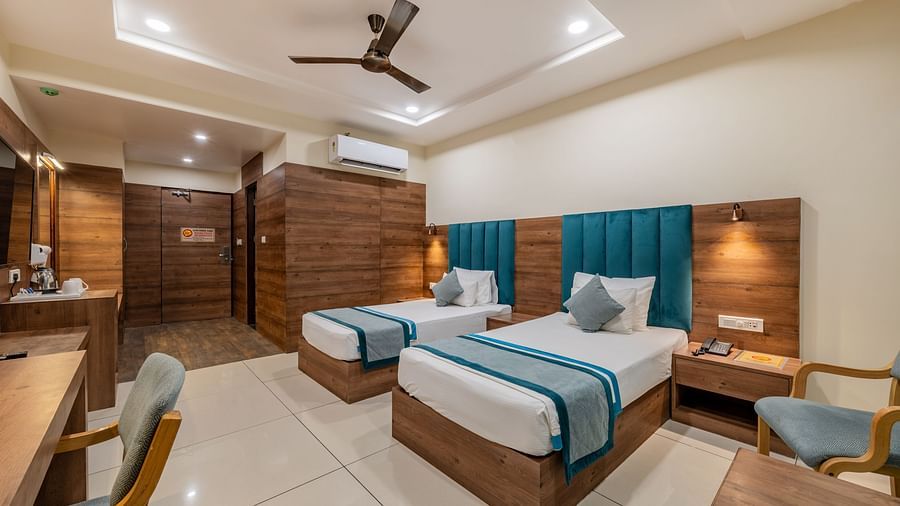View of a King twin bed room with polished flooring, teal padded headboards, seating area, work station, ceiling fan, and ambient ceiling lights at Hotel Highway King, Bilaspur.