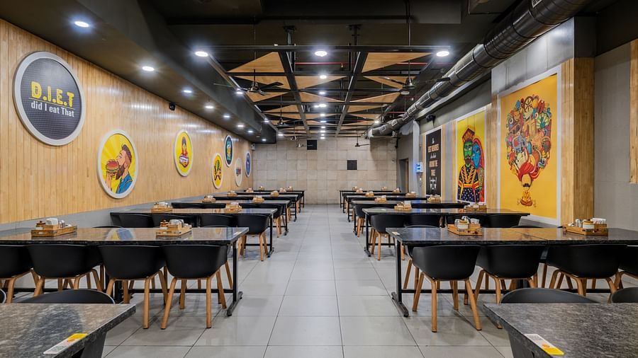 Circular food-themed artwork on wooden walls and symmetrical table arrangement at Hotel Highway King, Bilaspur.