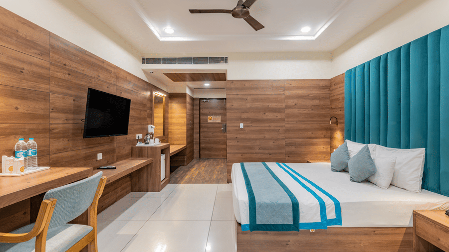 A spacious bedroom featuring a plush bed, wooden wall accents, a ceiling fan, and a work desk at Hotel Highway King, Bilaspur.