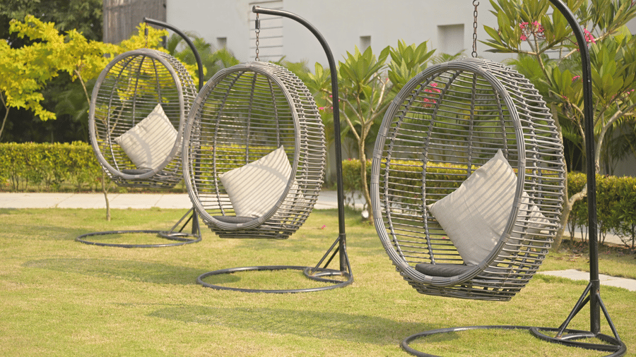 Row of 3 circular hanging chairs with cushions arranged on a wide green lawn at Hotel Sonar Bangla, Mayapur.