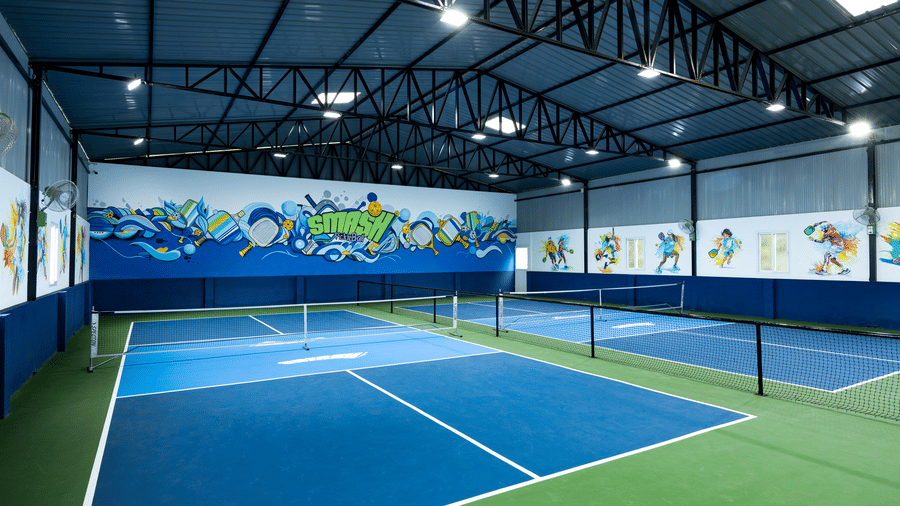Indoor pickleball courts with blue and green flooring and colourful wall art, located at Jenneys Residency, Coimbatore.