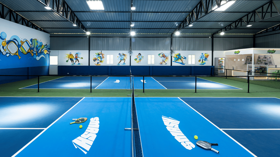 Indoor pickleball courts with paddles and balls on blue surfaces, located at Jenneys Residency, Coimbatore.