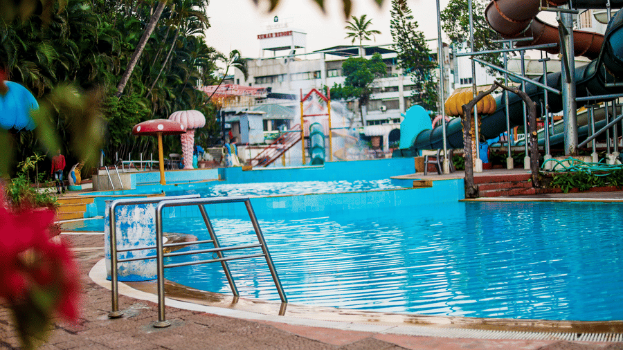 View of a swimming pool with metal railings along the edge and a water slide complex visible in the distance at Kumar Resort by Turtle.