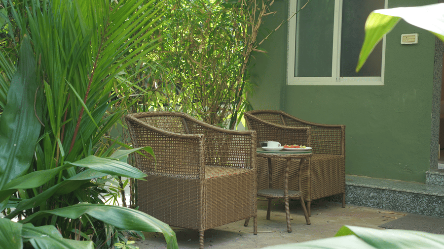 An outdoor seating area with 2 wicker armchairs and a small table surrounded by green plants at Oceanature Resort, Alibaug.