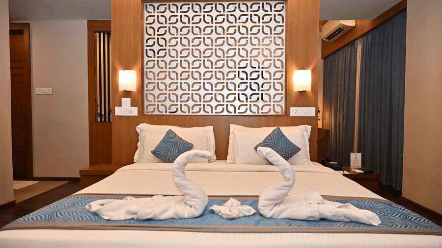 Suite bedroom with a bed dressed in white and blue linen, swan-shaped towel art, a patterned wall panel headboard and long blue curtains.