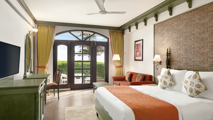 A bedroom with a queen size bed with a runner, a wall-mounted TV, and glass doors at Ramada by Wyndham Mussoorie Mall Road