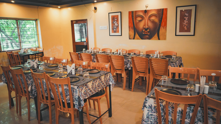 An indoor restaurant dining area with long tables, wooden chairs, and a large colourful Buddha painting on the wall.