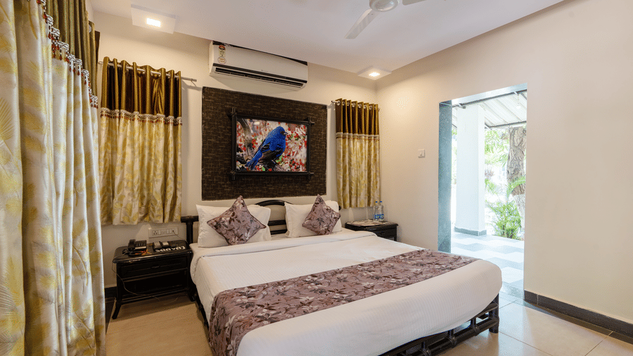 The Deluxe Cottage with a double bed, side tables, artwork hanging on the wall, an air conditioning, and an opening outside the room at Saavaj Resort.