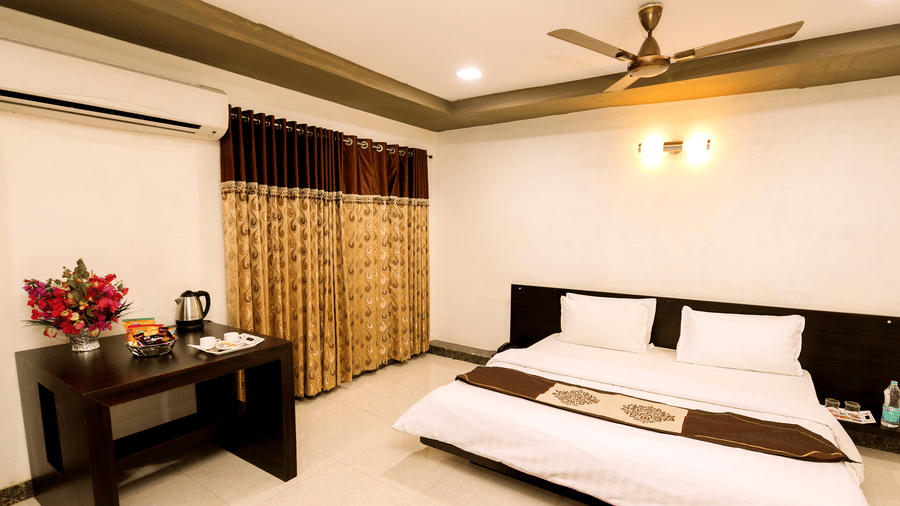 The Deluxe Room with with a double bed, a work desk, an air conditioning, a ceiling fan, a long window with draped windows, and tiled floor at Saavaj Resort.