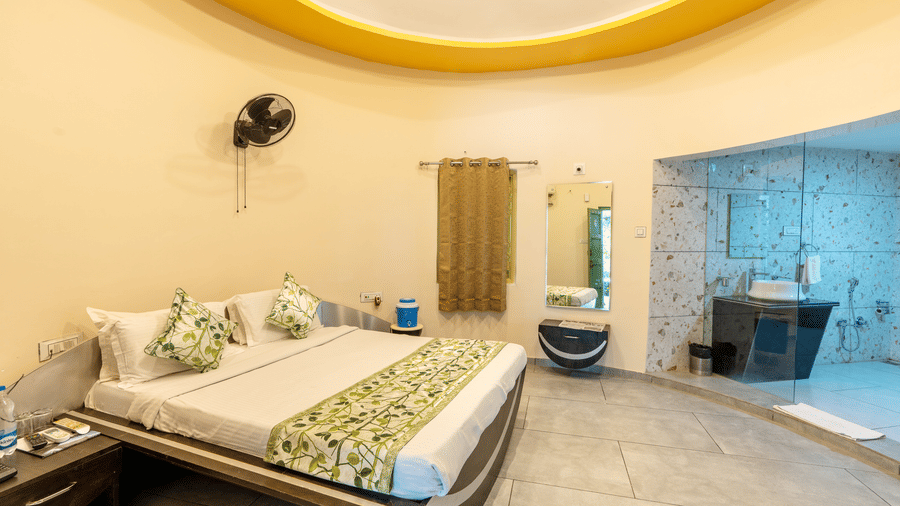 The Honeymoon Suite with a double bed, a wall-mounted fan, a mirror,  an opening towards the washroom and vanity area at Saavaj Resort.