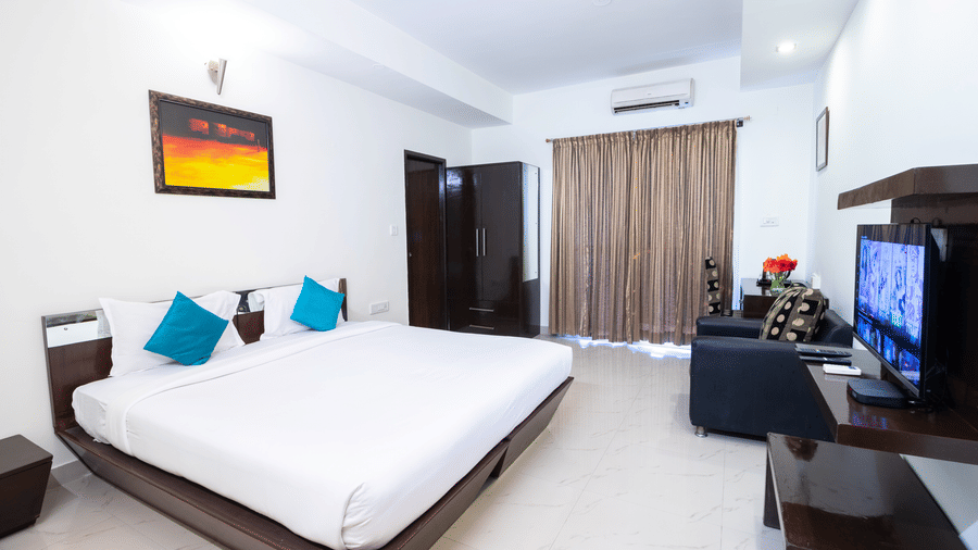 Air-conditioned room with double bed and teal pillows at Sanctum Suites Domlur Bangalore