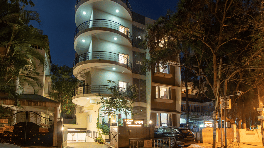 Night view of the hotel building with illuminated façade and curved architectural details at Sanctum Suites Indiranagar, Bangalore.