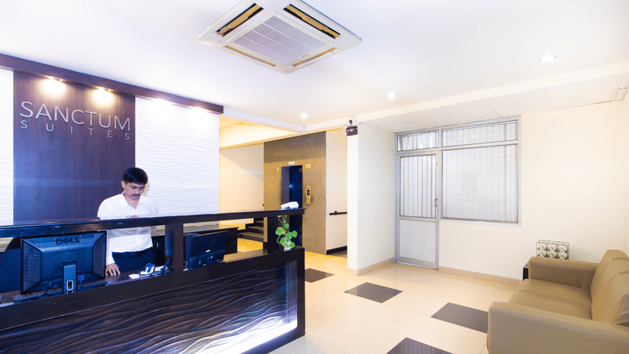 Hotel reception desk with dark interiors, a cassette air conditioner, and a tiled floor at Sanctum Suites Indiranagar, Bangalore.