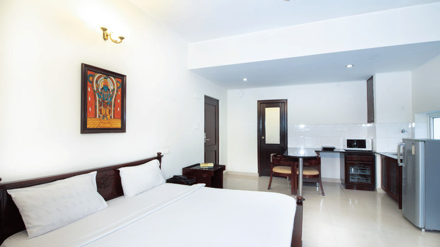 Bright hotel room with a double bed, a ceiling fan, and traditional wall art at Sanctum Suites Indiranagar, Bangalore.